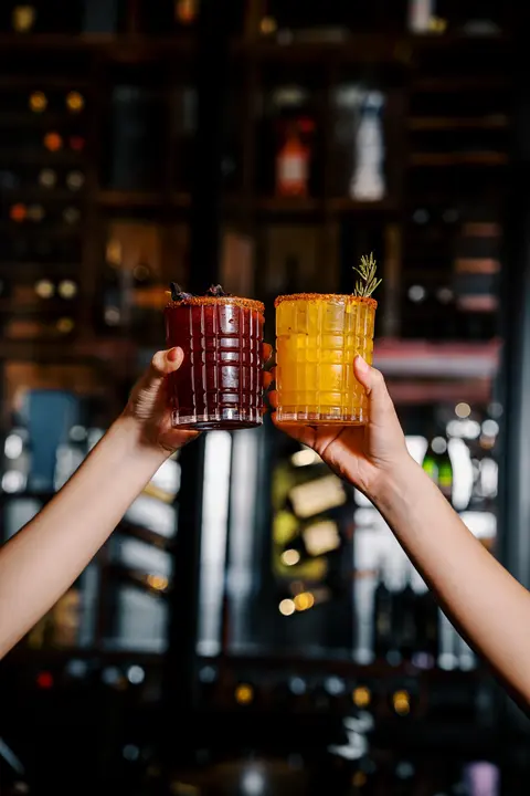 Brindis con dos cocteles de mezcal frente a la barra