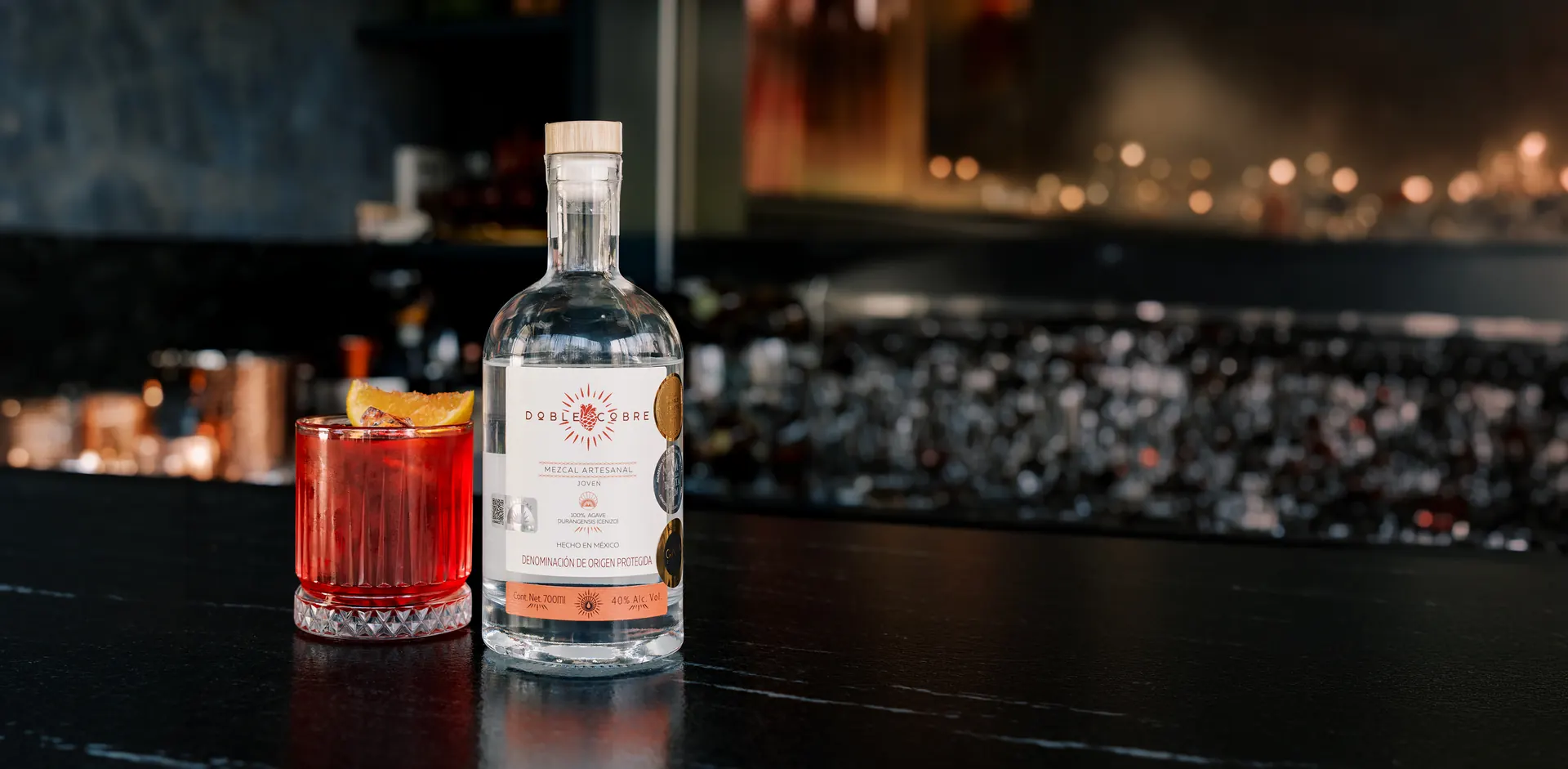 Botella de Mezcal Doble Cobre junto a un coctel de autor en la barra de un bar