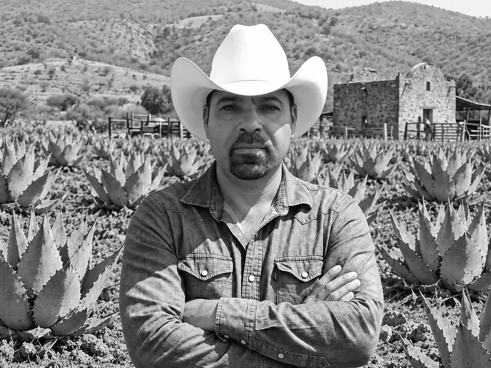 Mauro Débora Escobar, maestro mezcalero, con sombrero y los brazos cruzados entre agaves cenizo en Nombre de Dios, Durango