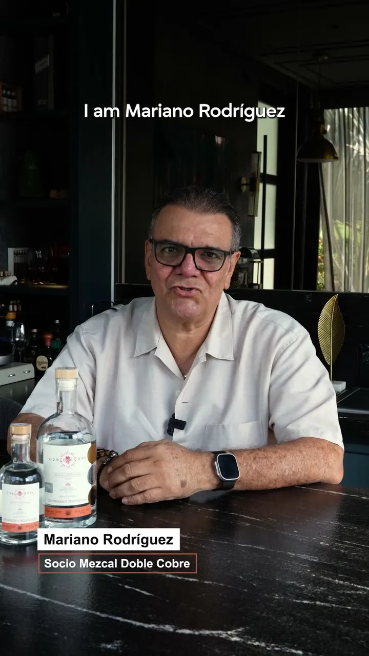 Mariano Rodríguez, partner at Mezcal Doble Cobre, seated behind two bottles of the mezcal