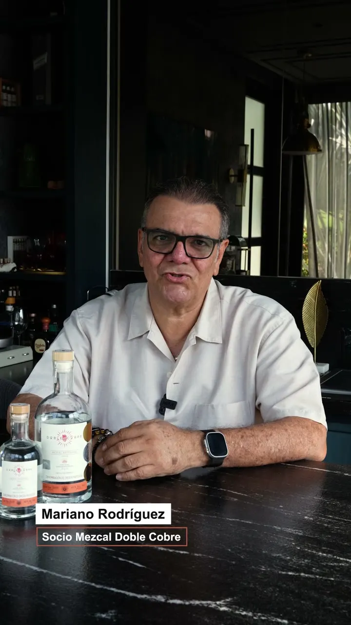 Mariano Rodríguez, socio de Mezcal Doble Cobre, sentado frente a dos botellas del mezcal