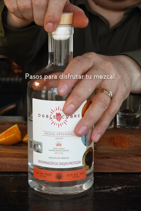 Manos destapando una botella de Mezcal Doble Cobre: pasos para disfrutar tu mezcal