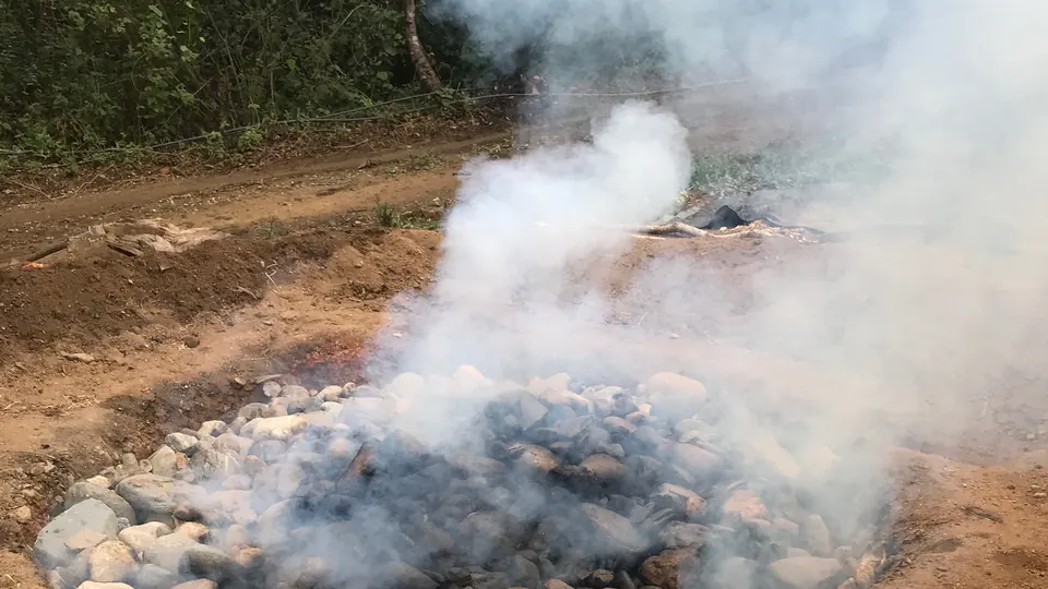 Horno prehispánico de tierra con piedra volcánica humeando durante la cocción del agave